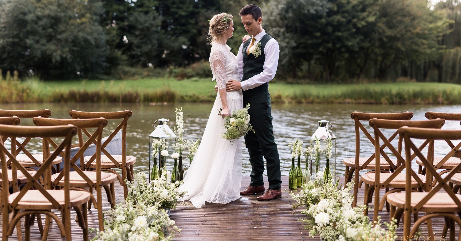 Bride and groom standing on jetty next to lake at Horsley Hale Farm, photo by Sarah Brookes Photography